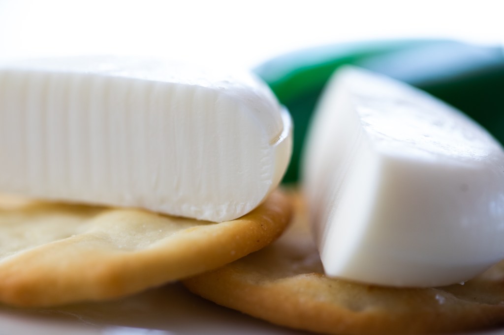 two crackers, each with half a plant-based babybel cheese round on it, with the green wax casing blurred in the background.
