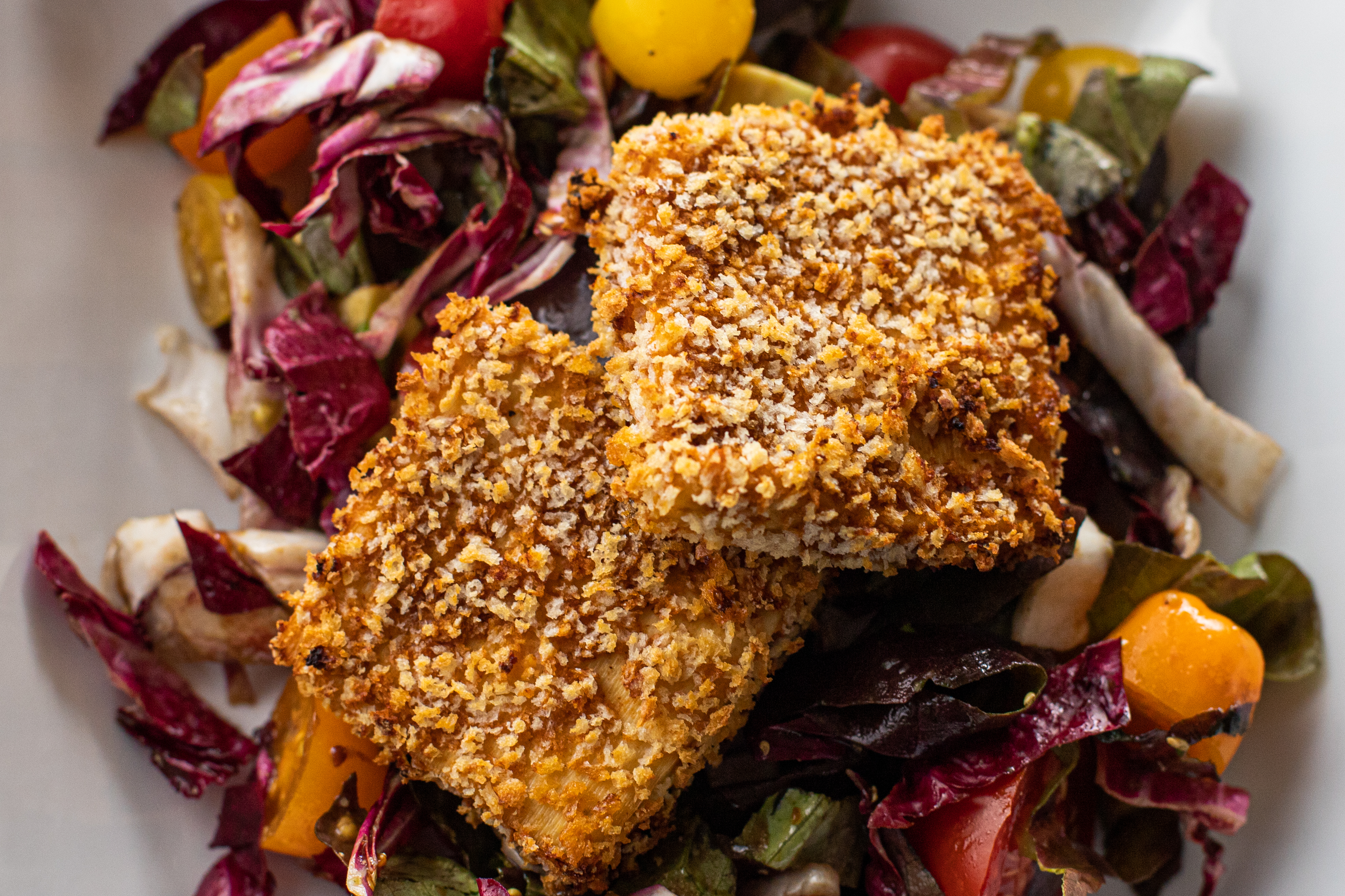 Two squares of panko-breaded tofu, air-fried to golden brown, sitting atop a salad of mixed greens, radicchio, and cherry tomatoes in a balsamic vinaigrette. Yum.