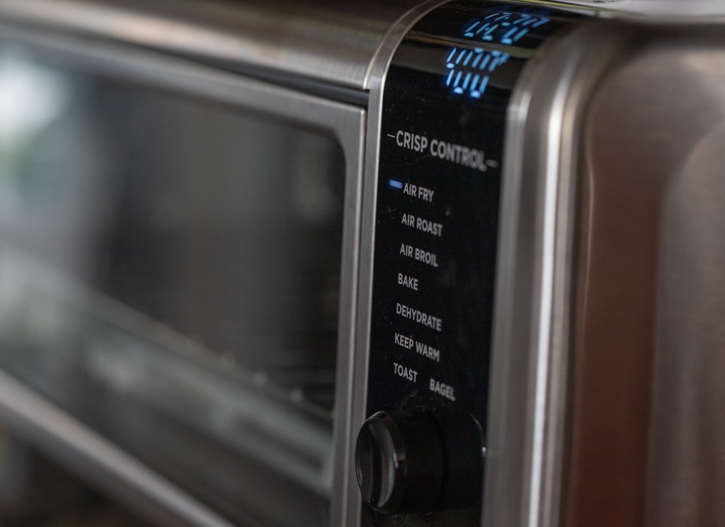 control panel of an oven-style air fryer, set to 0:20 minutes and 400 F on "air fry," with other options on the Crisp Control panel (not selected): Air Roast, Air Broil, Bake, Deyhdrate, Keep Warm, Toast, Bagel) and a dial. The interior of the oven is partially visible in blur in the background