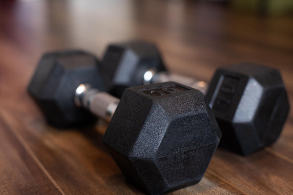 A pair of black hexagonal 10-pound dumbbells with steel handles, on a wood laminate floor. Photo by Tracy Isaacs