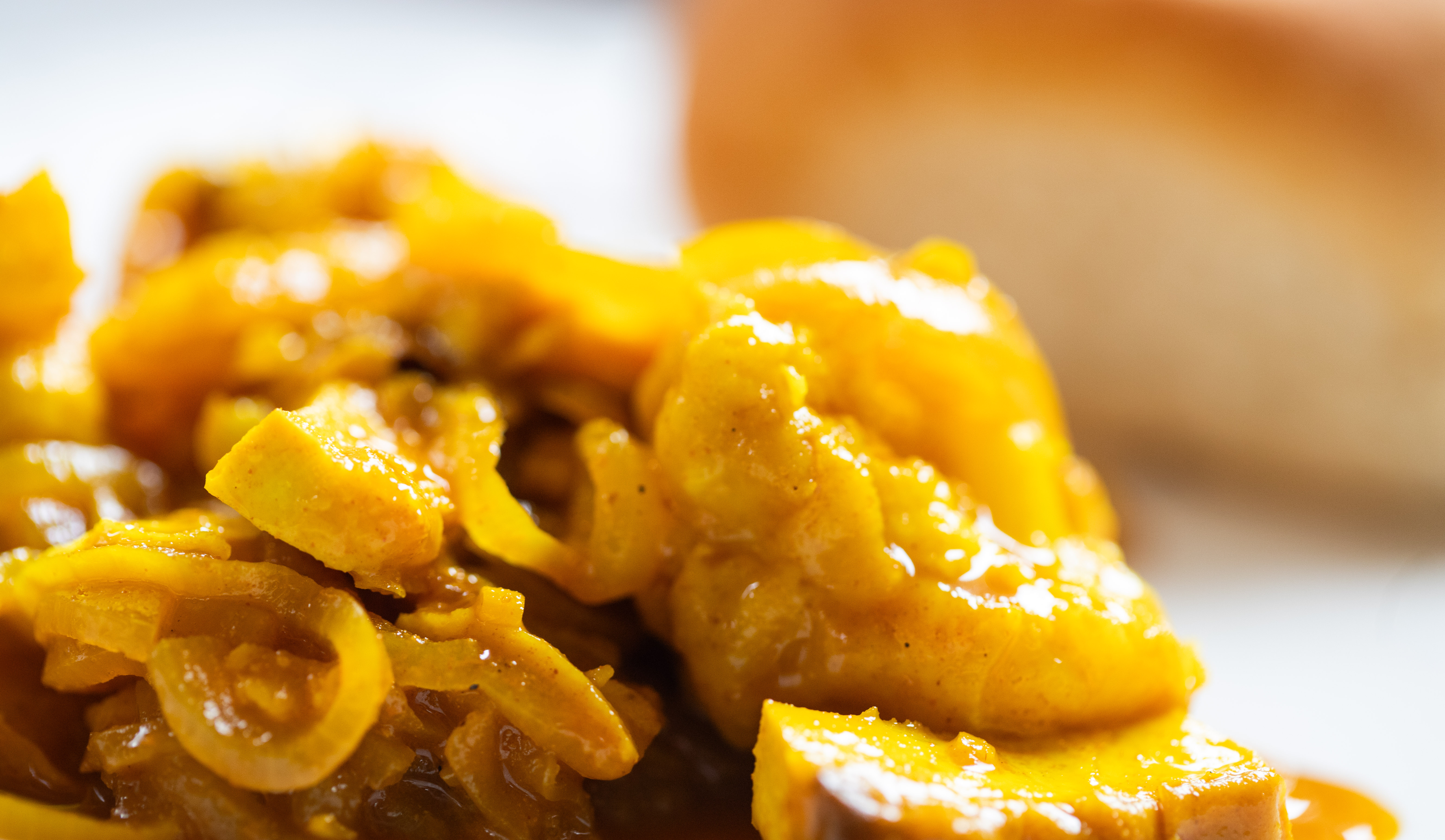 Veganized version of the South African curry dish called "pickled fish, here with tofu and cauliflower in an onion curry sauce, dinner roll blurred in the background. Photo by Tracy Isaacs