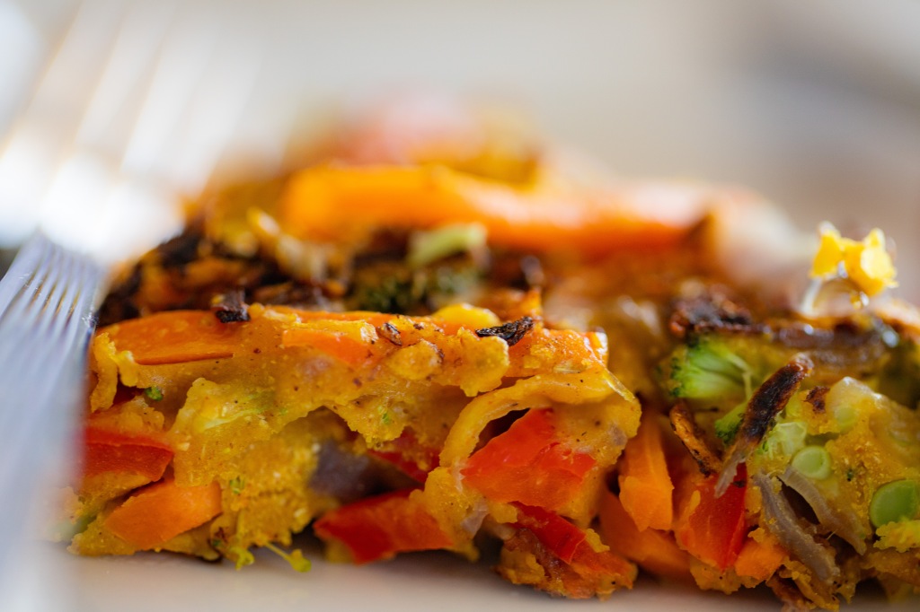 Close up of a savoury veggie pancake, side view, packed with carrots, peppers, broccoli, and onions, fork alongside. Yum! Photo by Tracy Isaacs