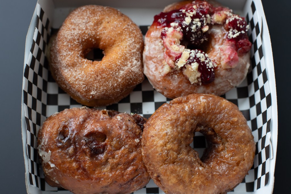 Overhead shot of four big (vegan!) donuts on a checkered paper in a box. Photo by Tracy Isaacs