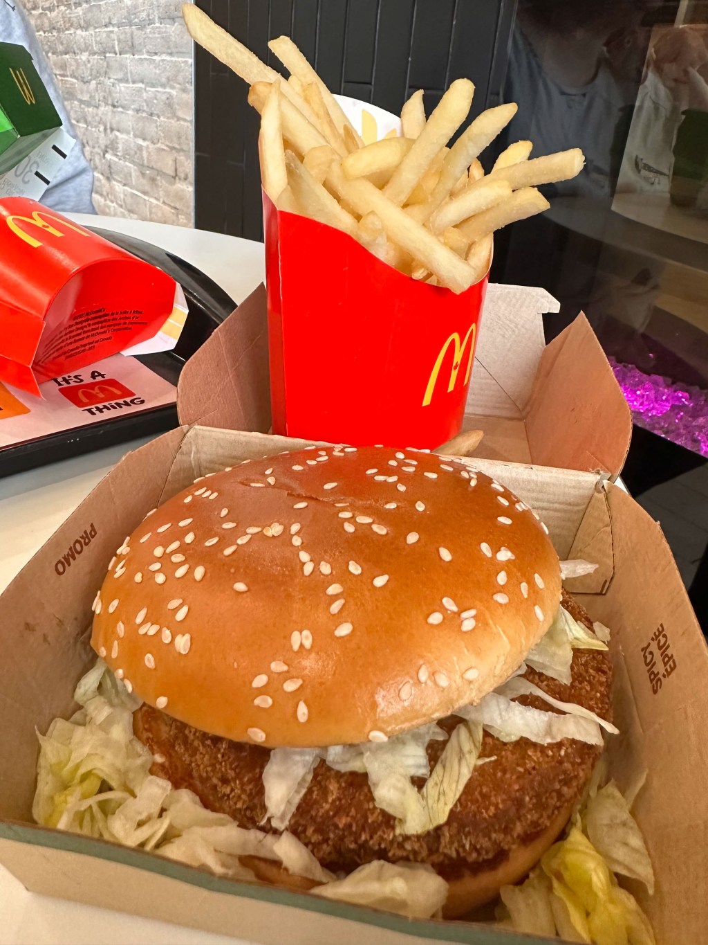close up of mcveggie burger with shredded lettuce on a sesame seed bun in a cardboard container, mcdonalds fries in the background.